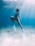 Freediver glides over sandy sea with white fins. Attractive woman free diver in blue ocean