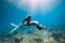 Freediver glides over sandy sea with white fins. Slim woman free diver in ocean