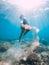 Freediver woman glides underwater with sand in hand. Free diver with fins posing in transparent sea