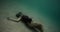 Freediver woman lying underwater bottom, filmed on cinema camera. Brutal girl in black suits against background of