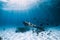 Freediver young woman with fins glides over sandy bottom with tropical fishes in transparent ocean