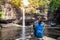 Freedom traveler woman alone sitting waterfall front on stone with bag and a beautiful nature.