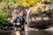 Freedom traveler woman standing waterfall front on stone with bag and camera enjoying a beautiful nature.