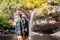 Freedom traveler woman standing waterfall front on stone with bag and camera enjoying a beautiful nature.