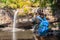 Freedom traveler woman standing waterfall front on stone with bag and Taking a picture by camera enjoying