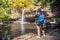 Freedom traveler woman standing waterfall front on stone with bag and Taking a picture by camera enjoying