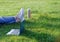 Freelance business concept. Woman legs on green grass lawn in city park, laptop and thermos