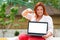 Freelance. Portrait of caucasian smiling woman holds a laptop and points at the screen with her finger. Plus size model. Outdoor.