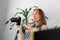 Freelance. A young woman is holding a camera and thinking about ideas for work. Indoor plant in the background. The concept of