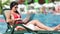 Freelancer girl in red swimsuit working on laptop pc lying on deck chair near swimming pool