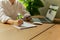 Freelancer hand holding cell phone and filling paperwork with laptop on table.