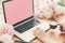 Freelancer. Hands working on stylish laptop with empty screen, coffee cup, notebook,phone, pink and white peonies on wooden table