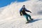 Freeride snowboarder rolls on a snow-covered slope leaving behind a snow powder against the blue sky