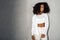 Freestyle. African girl in white outfit with bare belly standing isolated on gray looking aside pensive