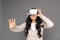 Freestyle. Mature lady in virtual reality headset standing on grey watching video touching space happy