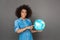 Freestyle. Mulatto woman standing isolated on grey with terrestrial globe pointing at continent smiling cheerful