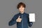 Freestyle. Teenager boy standing isolated on grey showing screen of digital tablet thumb up smiling happy