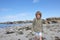 Freezing boy at low tide in the sand of a beach with seaweed, water and rocks in the background, summer holiday feeling