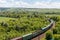 The freight railroad train rides through fields and hills amidst green meadows and trees