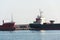 Freight truck stands between largo cargo ships in shipping harbor, oarsmen rowing in foreground sea, port Monopoli, Italy