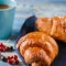 French breakfast: Ruddy croissants with forest berries and a cup of coffee with milk stand on a table