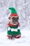 French Bulldog dog wearing a traditional cute christmas elf costume with arms holding present inwhite snow winter landscape