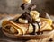 French crepes with bananas, topped with dark chocolate. Sweet breakfast. Wooden table