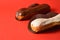 French desserts eclairs with white chocolate and dark chocolate on top filled with custard served on red background