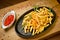 French fries with ketchup in a cast-iron pan with rosemary and pepper. On a wooden stand