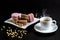 French macarons of three colors and a cup of hot fragrant espresso with scattered pine nuts on a blackbackground