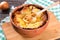 French onion gratin soup in a clay pot, authentic recipe, wooden spoon on a cutting board on an old rustic table, close-up