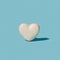 French patisserie minimal artisan concept. White heart shaped attractive macaron alone against pastel blue background