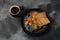 French toasts with fried plantains, dripping maple syrup, sugar powder on a black plate