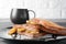 French toasts with fried plantains, dripping maple syrup, sugar powder on a black plate.