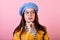 Frenchwoman lady in a stylish hat and beret and a yellow raincoat with glasses shows think on a pink background