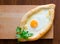 Fresh Ajarian khachapuri with egg and cheese on a wooden plate, Georgian cuisine, top view