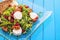 Fresh arugula salad with beetroot, goat cheese, bread slices and walnuts on glass plate on blue wooden background, product