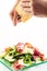 Fresh arugula vegetable salad with ham and cheese on glass plate on white background and cooks hands shredding cheese, pr