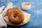 Fresh bagels with butter and cheese on plate and cup of coffee on blue background