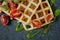 Fresh baked Belgian waffles with arugula, tomatoes and avocado on black a plate. Savory waffles. Breakfast concept. Healthy