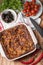 Fresh Baked Lasagne in Red Dish with Black Olives Tomatoes and Chilli on Wooden Table