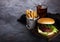 Fresh beef burger with sauce and vegetables and glass of cola soft drink with potato chips fries on stone kitchen table background