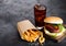 Fresh beef burger with sauce and vegetables and glass of cola soft drink with potato chips fries on stone kitchen table background