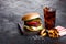 Fresh beef burger with sauce and vegetables and glass of cola soft drink with potato chips fries on stone kitchen table background