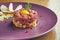 Fresh beef steak tartare with parmesan cheese, capers, croutons and yolk quail on a purple plate on a wooden background