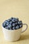 Fresh blueberries in a white ceramic cup on a yellow crackle background