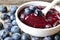 Fresh blueberry jam in a white bowl and freshly picked blueberries on a burlap background close up.