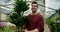 Fresh Botanicals: Young Man in Brown Sweater and Glasses Examining Large Lush Plant in Specialized Plant Shop