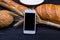 Fresh bread, flour, ears and a smartphone on a wooden table.