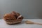 Fresh bread in a wicker basket - buns, baguette and ears of wheat on wooden table against gray background